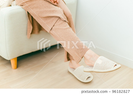 Feet of a woman wearing slippers sitting on a sofa in a room with floor heating 96182827