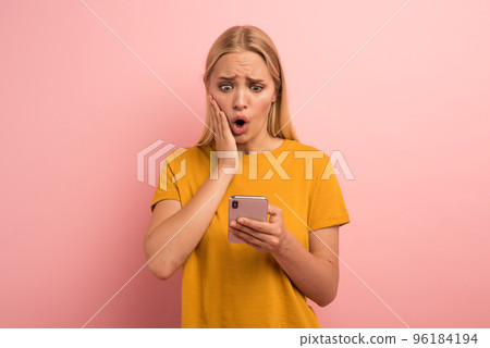 Blonde cute girl with her smartphone. Amazed and surprised expression face. Pink background Blonde cute girl with her smartphone. Amazed and surprised expression face. Pink background 96184194