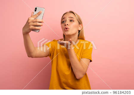 Blonde cute girl sends hearts on her smartphone. Happy and lovely expression face. Pink background 96184203