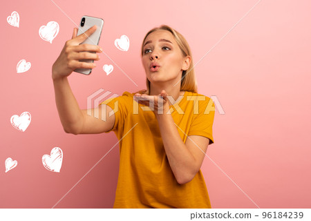 Blonde cute girl sends hearts on her smartphone. Happy and lovely expression face. Pink background 96184239