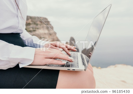 Silhouette of laptop and cup on the beach over sea sunset. Sparkling sea water on background. Freelancer, blogger working on notebook on the beach. 96185430