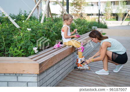 Caucasian woman helping her daughter put on roller skates. 96187007