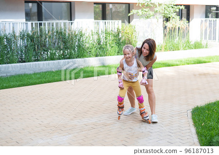 Caucasian woman teaches her daughter to skate on roller skates. 96187013