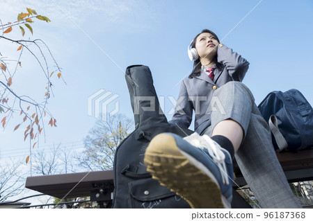 A high school girl wearing slacks who sits on a bench and listens to music Guitarist 96187368