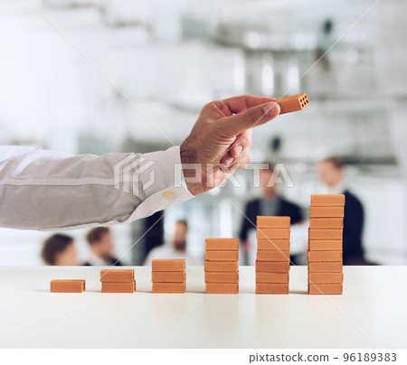 Businessman puts a brick on a bricks pile. Concept of growing statistics and success Businessman puts a brick on a bricks pile. Concept of growing statistics and success 96189383