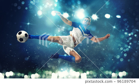 Soccer striker hits the ball with an acrobatic kick in the air on dark blue background Soccer striker hits the ball with an acrobatic kick in the air on dark blue background 96189704