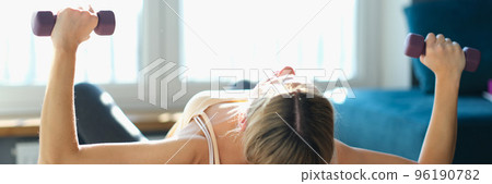 Young woman doing bench press with dumbbells and stabilizing ball at home Young woman doing bench press with dumbbells and stabilizing ball at home 96190782