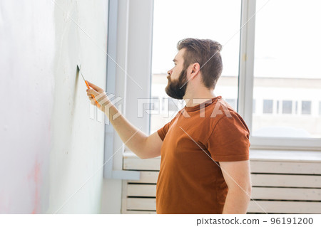 Young man using spatula and plastering of wall with white fresh finishing putty. Closeup. Repair work of home. Side view. 96191200