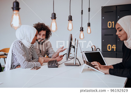 Group of multi-ethnic colleagues working on desktop computers, laptop and sharing their ideas in a modern office space.Young influencers work on online marketing projects. 96192929