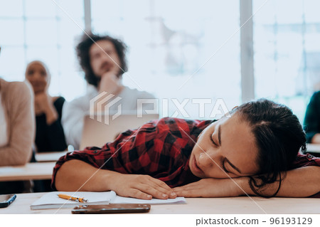 Tired woman napping on the table during a lecture in the classroom 96193129