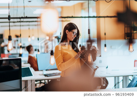 Female boss, manager executive posing in a modern startup office while being surrounded by her coworkers, team. Female boss, manager executive posing in a modern startup office while being surrounded by her coworkers, team. 96193409