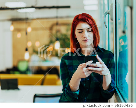Headshot portrait of modern woman in office at night near window using smartphone 96193486