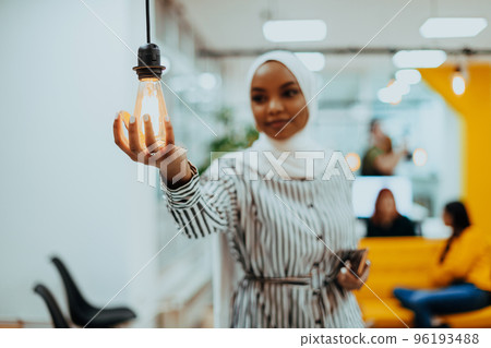 Sentimental portrait of African-American young female Muslim wearing hijab while holding a lightbulb. Sentimental portrait of African-American young female Muslim wearing hijab while holding a lightbulb. 96193488