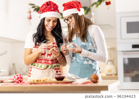 A mother and her teenage daughter dressed in Christmas aprons are making Christmas cookies at home in the kitchen 96194423