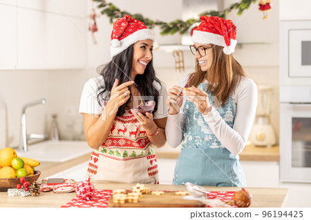 Daughter and mother make Christmas cookies from Linz. Mom tastes sweet jam and daughter spreads marmelade on a cookie. 96194425