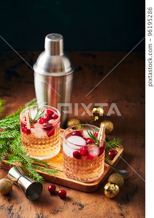 Alcoholic cocktail or non-alcoholic cocktail with vodka and cranberries with ice, shaker, jigger and bar spoon, fir branches and glowing garland for christmas on wooden background 96195286