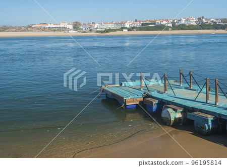 Small turquoise wooden pier at Praia das Furnas sand beach with view over the Mira river to Vila Nova de Milfontes, Vicentine Coast Natural Park Portugal. 96195814