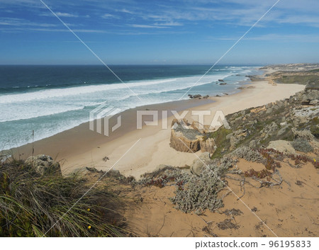 View of Praia dos Aivados sand beach with ocean waves and sharp rock and green vegetation at wild Rota Vicentina coast near Porto Covo, Portugal. 96195833