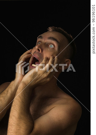 Shirtless man with frightened expression on black background. Portrait of a man with his hands on his face and mouth open. Shock at what he saw. Shirtless man with frightened expression on black background. Portrait of a man with his hands on his face and mouth open. Shock at what he saw. 96196101