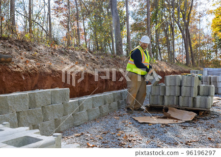 Man uses leveling tool during construction of concrete block wall to create retaining wall on new property Man uses leveling tool during construction of concrete block wall to create retaining wall on new property 96196297