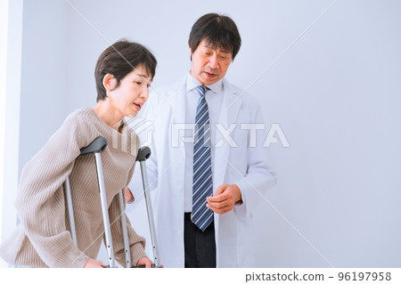 A middle-aged woman walking on crutches while being assisted by a doctor Rehabilitation image 96197958