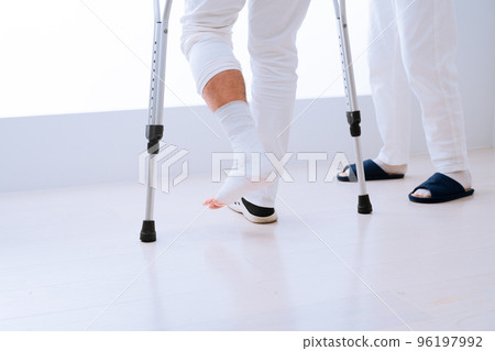 A middle-aged man walking on crutches while being assisted by a doctor Rehabilitation image 96197992