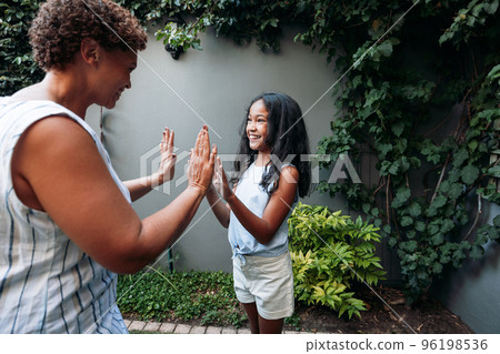 Granny and grandchild embrace and look at the camera. Grandma and granddaughter hugging and smiling while standing together outside. Granny and grandchild embrace and look at the camera. Grandma and granddaughter hugging and smiling while standing together outside. 96198536