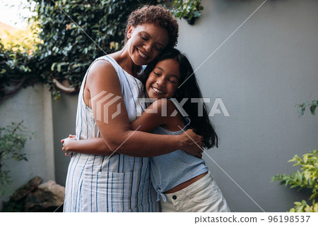 Smiling girl hugging her granny in the backyard. Grandmother and granddaughter are embracing with closed eyes. Smiling girl hugging her granny in the backyard. Grandmother and granddaughter are embracing with closed eyes. 96198537