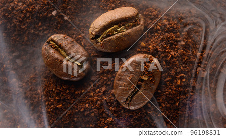 Three coffee beans lie on ground coffee, light aromatic coffee smoke. 96198831