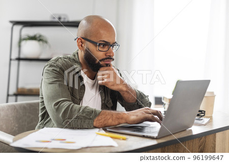 Portrait of concentrated male employee working on laptop at desk at home office, checking online project, copy space Portrait of concentrated male employee working on laptop at desk at home office, checking online project, copy space 96199647