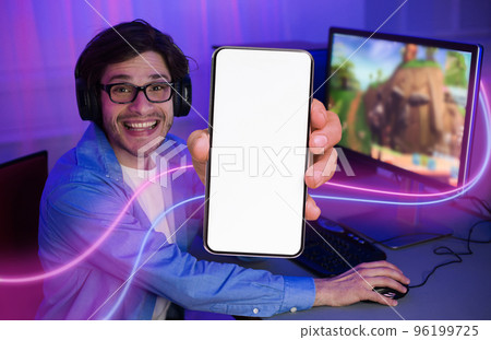 Cheerful guy playing video games on computer, showing smartphone Cheerful guy playing video games on computer, showing smartphone 96199725