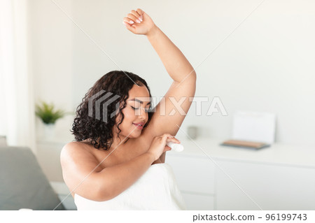 Young black body positive woman using antiperspirant stick for underarms, sitting in bedroom, free space Young black body positive woman using antiperspirant stick for underarms, sitting in bedroom, free space 96199743