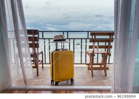 Travel suitcase and hat on the bedroom balcony with sea beach and chair for relaxing background, Travel, vacation concept. Travel suitcase and hat on the bedroom balcony with sea beach and chair for relaxing background, Travel, vacation concept. 96199804