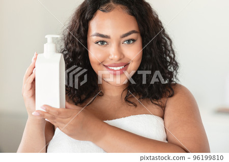 Beautiful black plus size woman holding bottle with moisturising body lotion, using new skincare product after bath Beautiful black plus size woman holding bottle with moisturising body lotion, using new skincare product after bath 96199810
