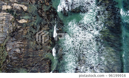 Waves break on the rocky shore of the Celtic Sea, top view. White foam on the waves. The coastline of the Atlantic. Turquoise water. Breathtaking seaside landscape. Aerial photo. Waves break on the rocky shore of the Celtic Sea, top view. White foam on the waves. The coastline of the Atlantic. Turquoise water. Breathtaking seaside landscape. Aerial photo. 96199916
