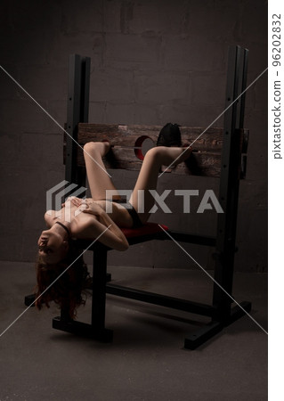 Alluring naked woman lying on BDSM chair 96202832