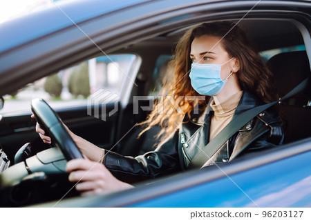 Young woman driving a car wearing on a medical mask during an epidemic. Transport isolation. Covid. Young woman driving a car wearing on a medical mask during an epidemic. Transport isolation. Covid. 96203127