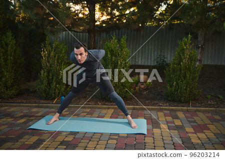 Full length of a determined male athlete, sportsman standing barefoot on a yoga mat, doing body stretching exercises, practicing a body weight training at sunset. Sport. Fitness. Outdoor workout 96203214