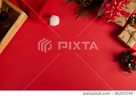 Christmas background with copy advertising space. Beautiful gifts with wrapping materials, decorative tapes, rope and Santa's hat on a red surface. Boxing Day. Packing presents. Mockup. Festive mood 96203249