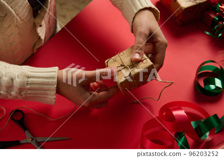 Craftswoman tying up a Christmas gift in a wrapping paper with deer pattern, tying bow using a linen rope. Boxing Day. Diy presents. New Year preparations. Step by step packing presents. Festivity Craftswoman tying up a Christmas gift in a wrapping paper with deer pattern, tying bow using a linen rope. Boxing Day. Diy presents. New Year preparations. Step by step packing presents. Festivity 96203252