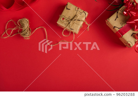 Beautiful presents, wrapped in a wrapping paper with deer pattern and tied up with linen rope and red tape, on top of a red background with copy advertising space. Christmas and New Year preparations 96203288