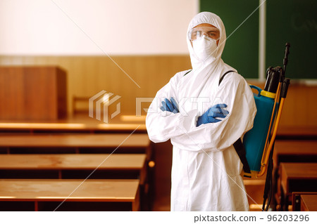 Portrait of man in protective hazmat suit with spray chemicals disinfecting school class. COVID-19. Portrait of man in protective hazmat suit with spray chemicals disinfecting school class. COVID-19. 96203296