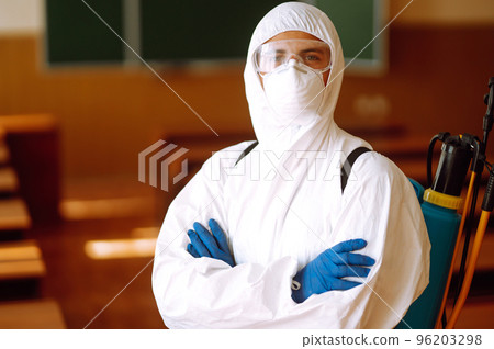 Portrait of man in protective hazmat suit with spray chemicals disinfecting school class. COVID-19. 96203298