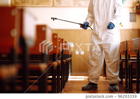 Man wearing protective suit disinfecting school class with spray chemicals to preventing the spread. 96203339