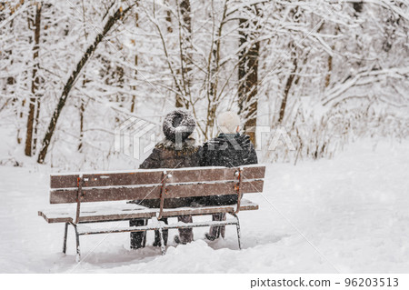 Senior couple sitting on bench, snowy winter weather. Concept of retirement age, family, love, Christmas 96203513