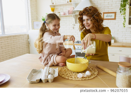 Mother and daughter prepare a cake together in the kitchen Mother and daughter prepare a cake together in the kitchen 96207035