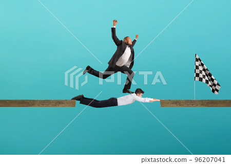 Businessman uses his body like a bridge to help his coullague to reach the flag. concept of teamwork and partnership. Cyan background 96207041