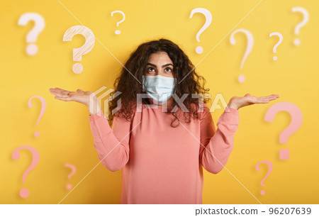 Girl with face mask has a lot of question about covid 19. Yellow background 96207639