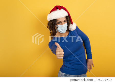 Woman with Christmas hat is optimistic about the defeat of covid 19 coronavirus. yellow background. Woman with Christmas hat is optimistic about the defeat of covid 19 coronavirus. yellow background. 96207698