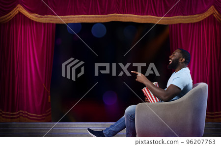 Man sitting on a armchair watches a show in a theatre 96207763